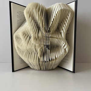Op de afbeelding: Een boekkunst sculptuur in de vorm van een vlinder, gemaakt door de pagina's van een boek te vouwen. Het boek is open en de pagina's zijn gevouwen tot een driedimensionale vorm.