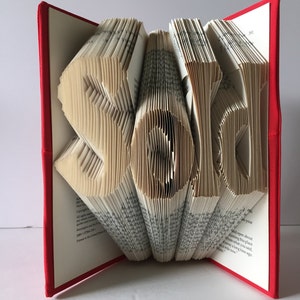 May include: A book with the word "Sarah" folded into the pages. The book is red and has a white spine. The pages are folded to create the letters of the name.