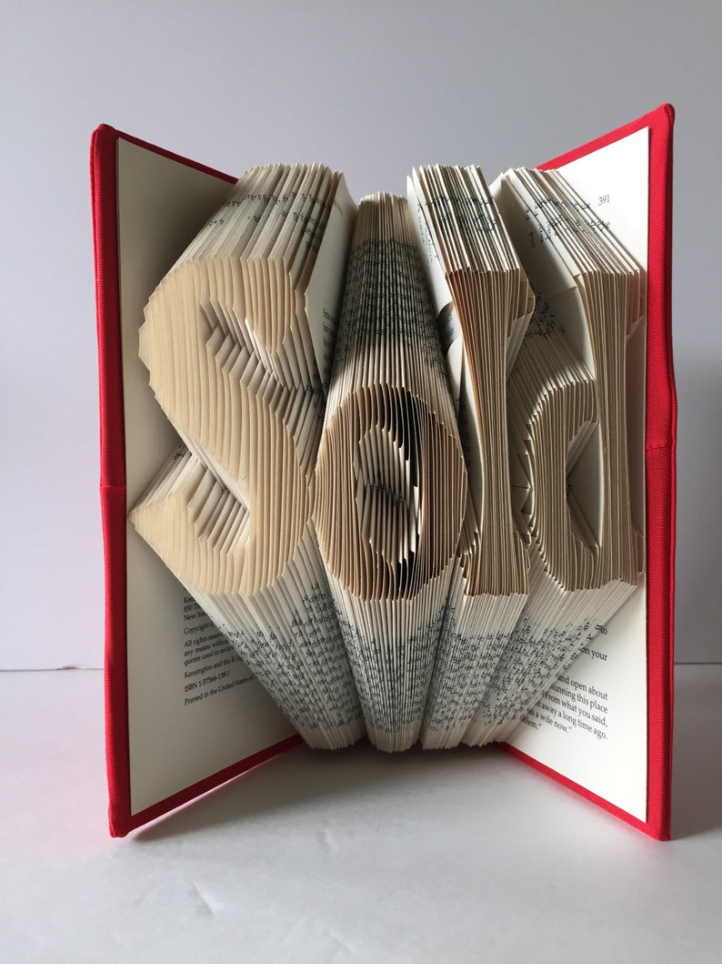May include: A book with the word "Sarah" folded into the pages. The book is red and has a white spine. The pages are folded to create the letters of the name.