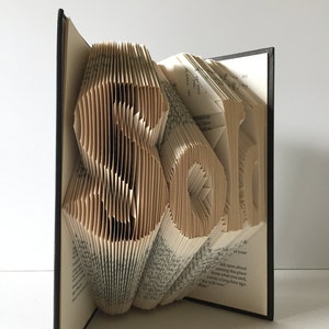 May include: A book art sculpture of the word "Roll" created by folding the pages of a book. The book is bound in black and the pages are a cream color.