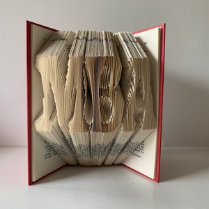 May include: A book with the name "VERA" folded into the pages. The book has a red cover.