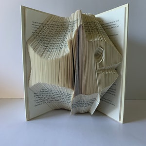 May include: A book folded into the shape of a bird. The book is open and the pages are folded to create the shape of the bird. The book is made of white paper and has black text on the pages.