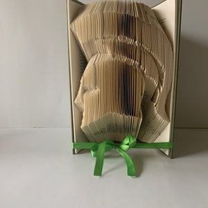 May include: A book folded into the shape of a human head, with a green ribbon tied around the base.
