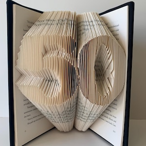 May include: An open book with pages folded to create the number "50". The book has a dark blue cover and the pages are beige with printed text. A unique, handcrafted decorative item.