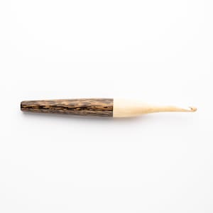 May include: A wooden crochet hook with a brown and black handle and a natural wood hook.