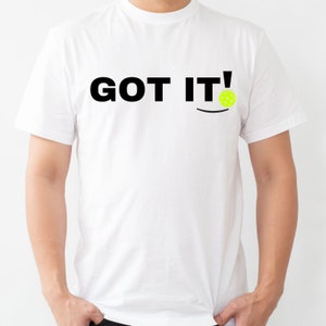 Puede incluir: Camiseta blanca con texto negro que dice "GOT IT!" y un gráfico de pickleball amarillo.