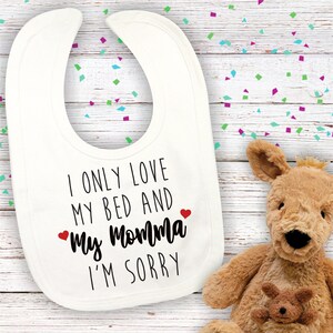 May include: White baby bib with black text that reads "I only love my bed and my momma I'm sorry" with two red hearts.