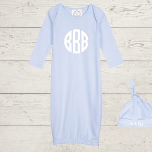 Puede incluir: Una bata de bebé azul claro con mangas largas y un monograma blanco de las letras "BBB" en un círculo en la parte delantera. Se incluye un gorro a juego de color azul claro anudado con el nombre "Bobby" bordado en blanco.