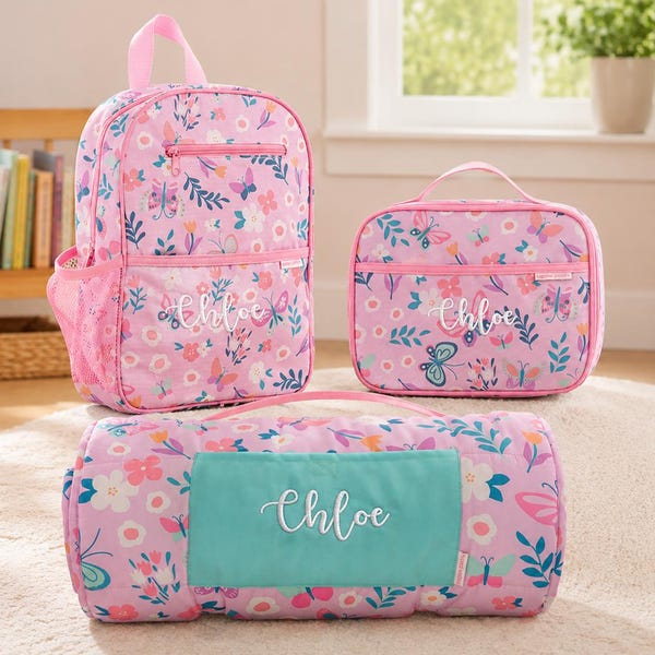 Könnte beinhalten: Ein rosa Rucksack, eine rechteckige Lunchtasche und eine gerollte Matte mit Blumen- und Schmetterlingsmuster. Jeder Artikel ist mit dem Namen Chloe in weißer Schreibschrift personalisiert. Die Matte hat ein türkisfarbenes, rechteckiges Feld.
