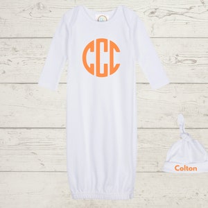 Puede incluir: Batista blanca para bebé con mangas largas y un gran monograma circular naranja con las letras CCC. También se incluye un gorro blanco anudado con el nombre Colton en letras naranjas.