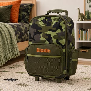 May include: A rolling backpack with a camouflage pattern in shades of green, brown, and black. The name "Bladin" is printed in orange on the front pocket. The backpack has a mesh pocket and side pockets. The wheels and handle are visible.