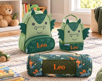 May include: A green dragon-themed backpack, a matching lunch bag, and a rolled-up blanket, all personalized with the name Leo in orange embroidery. The backpack and lunch bag feature dragon wings, horns, and scales, while the blanket has a dragon print.