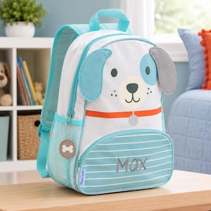K&ouml;nnte beinhalten: Ein wei&szlig;-blauer Rucksack mit einem Hundegesicht-Design. Der Rucksack hat blaue Akzente, einen Griff und eine Vordertasche mit dem aufgestickten Namen "Max". Er hat einen Knochen-Rei&szlig;verschluss.