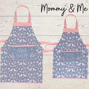 May include: A set of two pink and gray aprons with a whimsical unicorn and ornament pattern. The larger apron has a pocket with the text "Just a Pinch of Magic" and the smaller apron has a pocket with the text "Bake Some Magic".