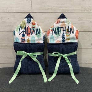 two blue towels with green ribbons tied around them, each with a name printed on it.