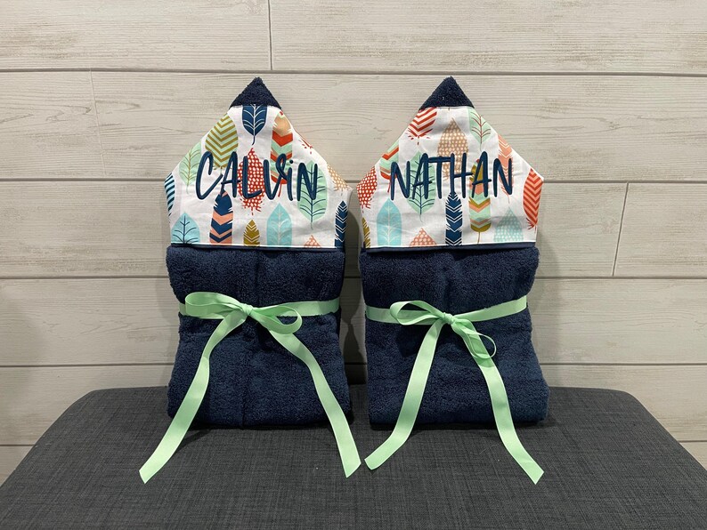 two blue towels with green ribbons tied around them, each with a name printed on it.