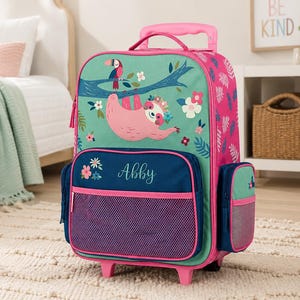 May include: A wheeled backpack in pink and teal, decorated with a sloth, toucan, and flowers. The front pocket is navy blue with the name "Abby". It has a retractable handle and wheels. The bag is designed for children and is suitable for travel.