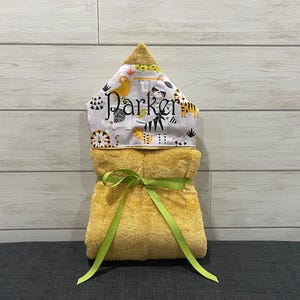 A yellow towel with a green ribbon tied around it, placed on a gray surface against a white wooden background.