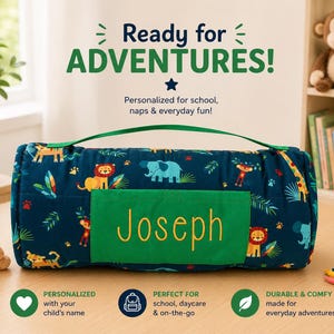 May include: A dark blue nap mat featuring a colorful jungle animal pattern with lions, elephants, and monkeys. A green rectangular pocket on the front displays the name Joseph in yellow text. The mat includes a green carrying handle.