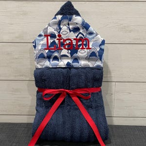 A towel with a shark pattern and the name "Liam" written on it, tied with a red ribbon.