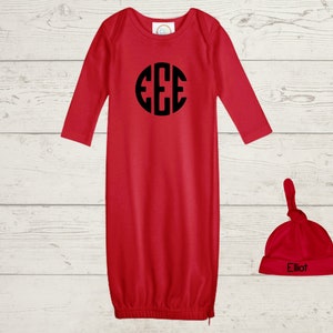 Puede incluir: Bata de bebé roja de manga larga con un monograma negro "EEE" en la parte delantera. Un gorro rojo atado a juego con el nombre "Elliot" bordado en negro.