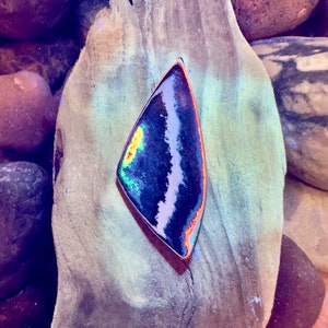 May include: A black and white agate pendant with iridescent rainbow colors, set on a piece of driftwood.