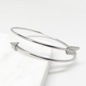 May include: A silver double-wrap bangle bracelet with an arrowhead design. The bracelet is open and has a simple, minimalist style.