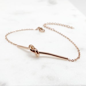 May include: A rose gold bracelet featuring a knot design and a delicate chain.