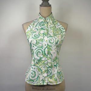May include: White halter top with a green and light green floral pattern. The top has a button-down front and a high collar. The garment is displayed on a mannequin.