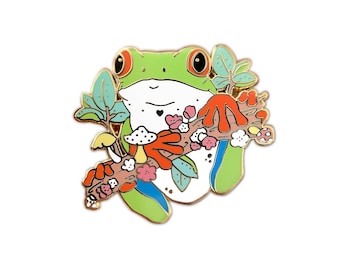 Op de afbeelding: Groene en witte kikker met rode ogen die een tak vasthoudt met roze bloemen en oranje paddenstoelen. De kikker zit op een tak met groene bladeren.