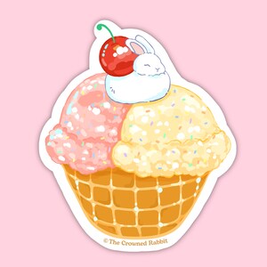 Peut inclure: Un lapin blanc avec une cerise sur la t&ecirc;te est assis sur un lit de cr&egrave;me glac&eacute;e rose et jaune dans un cornet gaufr&eacute;. La cr&egrave;me glac&eacute;e est recouverte de p&eacute;pites color&eacute;es. L'image est un autocollant avec le texte "The Crowned Rabbit" en bas.