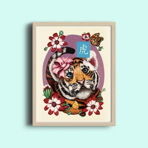 K&ouml;nnte beinhalten: Eine gerahmte Illustration eines Tigerjungen mit einer rosa Schleife. Der Tiger ist von roten Blumen und einem Schmetterling umgeben. Das chinesische Schriftzeichen f&uuml;r "Tiger" ist in Blau auf einem wei&szlig;en Quadrat geschrieben.