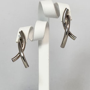 Peut inclure: Une paire de boucles d'oreilles en argent en forme de nœud sur un présentoir blanc.