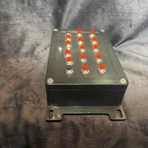 May include: A black box with 16 red buttons. The box has a metal bracket on each side.