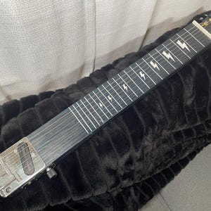 May include: A black steel-bodied guitar with a black fretboard and white lightning bolt inlays. The guitar has a silver pickup and a silver control knob.