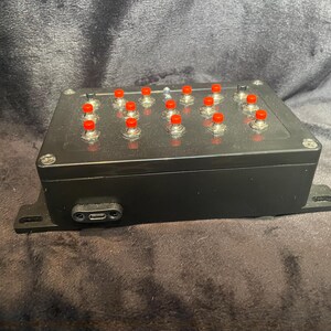 May include: A black box with a row of red buttons. The box has a USB-C port on the side.