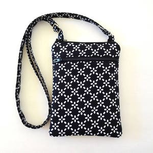 Op de afbeelding: Zwarte en witte crossbody tas met een bloemenpatroon. De tas heeft een ritssluiting aan de bovenkant en een lange, verstelbare riem. De tas is ongeveer 20 cm hoog en 15 cm breed.