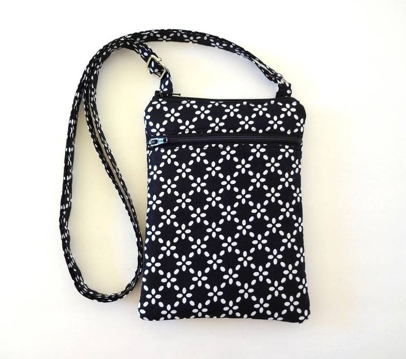Op de afbeelding: Zwarte en witte crossbody tas met een bloemenpatroon. De tas heeft een ritssluiting aan de bovenkant en een lange, verstelbare riem. De tas is ongeveer 20 cm hoog en 15 cm breed.