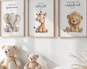 May include: Three framed watercolor prints with animal illustrations: an elephant, giraffe, and lion. Each print has a scripture quote. Two teddy bears sit on a white dresser below the prints. A white pillow and decorative plant complete the scene.