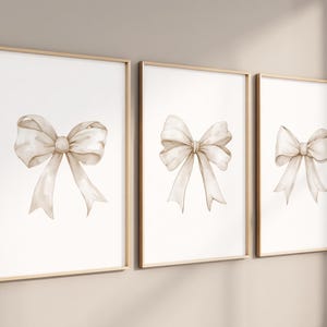 Op de afbeelding: Drie ingelijste prints met aquarel illustraties van beige strikken op een witte achtergrond.