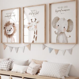 May include: Three framed art prints with animal illustrations. The first features a lion, the second a giraffe, and the third an elephant. Each print has a wooden frame and includes inspirational text. A garland of small flags hangs below the frames, and pillows rest on a wooden bench.