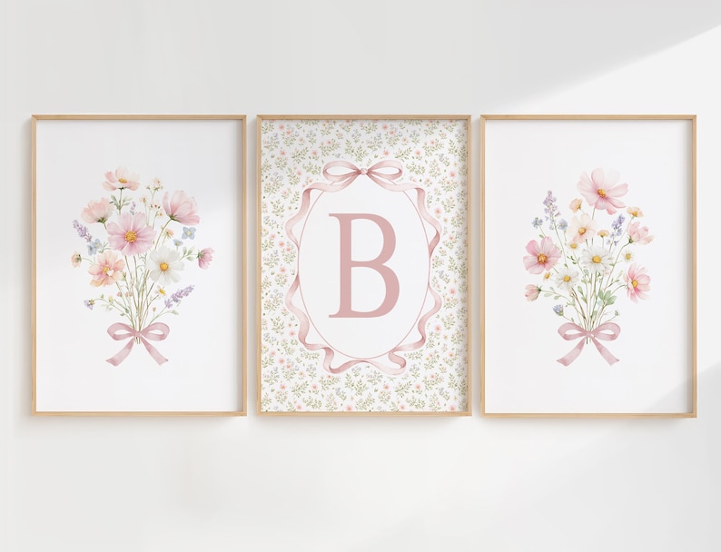 May include: Three framed floral art prints. Two prints feature watercolor bouquets of pink, white, and lavender flowers tied with pink ribbons. The center print has a pink letter "B" inside a pink ribbon frame.