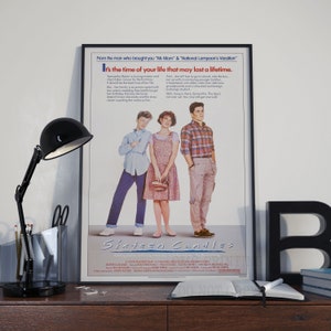 May include: A film poster for the movie Sixteen Candles, featuring three teenagers standing in front of a white background. The poster has the title of the film in large, bold letters at the bottom. The text above the title reads "From the man who brought you 'Mr. Mom' & 'National Lampoon's Vacation'. It's the time of your life that may last a lifetime."