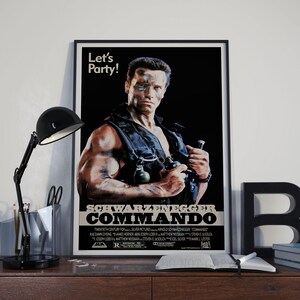May include: A black and white movie poster for the film "Commando" starring Arnold Schwarzenegger. The poster features a close-up of Schwarzenegger's face with a determined expression. The text "Let's Party!" is at the top of the poster. The poster also includes the film's title, "Commando", and the actor's name, "Schwarzenegger".