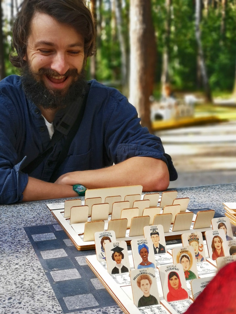 Board game fans. Laughing man in the park playing modern Guess Who made in wood.