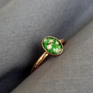 May include: A gold-colored ring with an oval-shaped, green and white stone. The ring's band has a textured appearance. The stone is set in a gold bezel, creating a striking contrast. The ring is a piece of jewelry.
