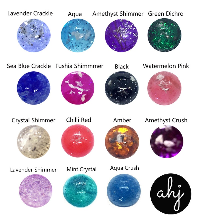 May include: A collection of fourteen circular cabochons in various colors and textures, including Lavender Crackle, Aqua, Amethyst Shimmer, Green Dichro, Sea Blue Crackle, Fushia Shimmmer, Black, Watermelon Pink, Crystal Shimmer, Chilli Red, Amber, Amethyst Crush, Lavender Shimmer, and Mint Crystal, with a black circular logo featuring the white text ahj.