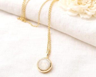 May include: A gold chain necklace featuring a circular pendant with a smooth, polished gold rim and a textured, shimmering white center. The delicate metal chain connects to the top of the round pendant, creating a simple and elegant jewelry piece.