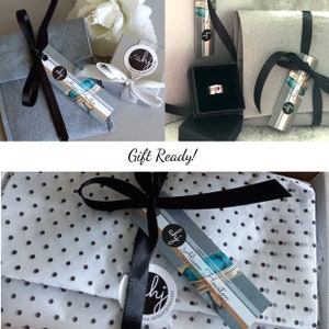 May include: A silver ring with a pink stone inside a black box, accompanied by grey felt pouches and white tissue paper with black polka dots. Each item is tied with black or white ribbon and features a tag labeled Alison Houston ahj.