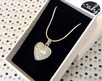 May include: A silver heart-shaped pendant necklace with a white, sparkly, resin-like filling. The necklace is displayed in a white box with a black interior.